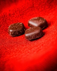 Wall Mural - Three dark chocolates arranged on a red textured background.