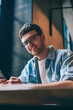 © BullRun - Portrait of successful millennial hipster guy in spectacles holding cellphone in hands and looking at camera, positive smiling male teenager using new smartphone for chatting and communication