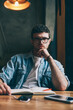 © BullRun - Portrait of confused hipster guy sitting at desktop spending time for autodidact and looking at camera, concentrated puzzled man in eyeglasses preparing for exam and doing school homework indoors