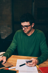 Fototapete - Serious male graphic designer creating logotyp for company using laptop device and good internet connection for work, young employee searching information on netbook sitting at wooden desktop