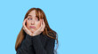 © Iryna - Woman displaying boredom with her chin resting on her hands against a blue background in a studio setting
