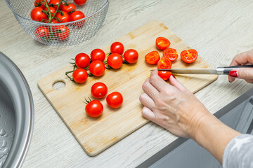 housewife cutting cherry tomato with knife on wooden board, top view. woman's hand cutting cherry tomato with a knife. making tomato soup. cooking tomato salad. cherry tomatoes in the kitchen. slicing