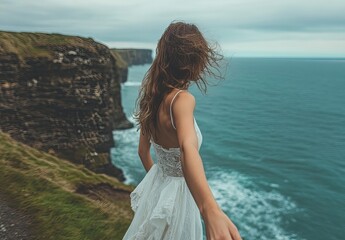 Wall Mural - an Italian woman in a white dress holding hands with a man, as they walk on a cliff overlooking the sea.