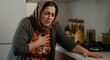 © gn8 - Middle eastern woman experiencing chest pain in home kitchen setting - health and heart condition concept