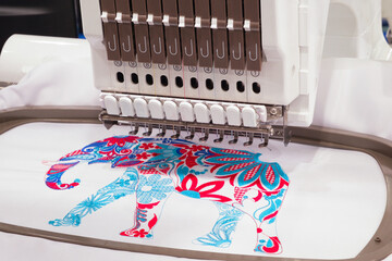 Poster - A machine is embroidering a design of an elephant. The machine has a lot of buttons and a lot of thread