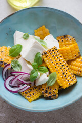 Wall Mural - Turquoise bowl with feta cheese and grilled corn salad, vertical shot, close-up, selective focus