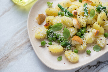 Wall Mural - Potato gnocchi served with different types of cheese, green peas and basil, horizontal shot on a white stone surface, closeup