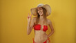 © Krakenimages.com - Attractive young woman in a red bikini and sun hat posing with a peace sign against an isolated yellow background.