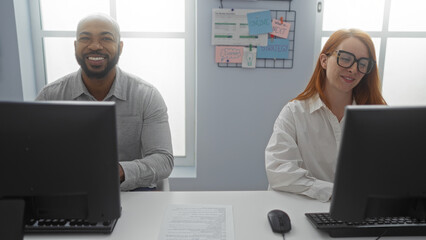 Man and woman working together at office desks with computers in a brightly lit workplace involving strategy planning notes on wall