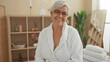 © Krakenimages.com - Beautiful grey-haired woman smiling in a wellness spa room wearing a white robe, surrounded by serene decor and soft lighting, indicating relaxation and beauty treatment