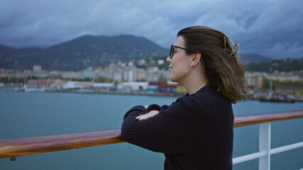 Wall Mural - Woman enjoying scenic view from cruise ship dock with mountains and ocean in background, wearing sunglasses and black sweater, relaxed and smiling.