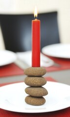 Wall Mural - A red candle stands atop stacked stones on a plate, creating a simple centerpiece.