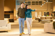 © Dejan - A couple is caught in an engaging moment as they point in interest while exploring a well-furnished showroom, surrounded by elegant lighting and stylish sofas.