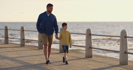 Wall Mural - Father, son and holding hands at sea on holiday, walking and outdoor for bonding with daddy. Boy, child and papa for vacation security on promenade, together and ocean for love or connect on trip