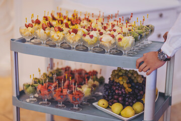 Hands of waiter in gloves serves sweets. Catering, many small cakes, sweets, fruits served on plate for party. Candy bar on birthday or wedding holiday dinner. tasty dessert.Restaurant service