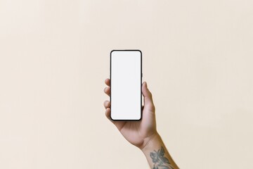 Poster - Person holds smartphone with blank screen. Studio shot. Light beige background. Hand displays modern device. Image shows person displaying new smartphone. Blank screen tech device perfect for
