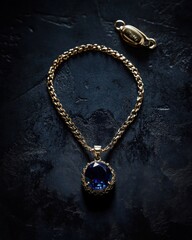 Aufkleber - Gold chain necklace with blue gem, clasp, on dark surface.