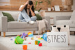© Pixel-Shot - Depressed young mother sitting on sofa among scattered children's toys at home, focus on paper sheet with word STRESS