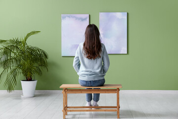 Wall Mural - Young woman on bench looking at paintings at art gallery, back view