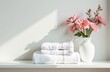 © Margarita Serenko - stacked bath towels and beautiful flowers on white table in bathroom. Space for text