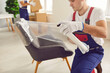 © Studio Romantic - Male worker from removal service or delivery company wrapping furniture before transportation. Man in uniform workwear wrapping stylish armchair with sticky self clinging protective transparent film