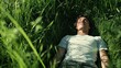 © milenialdesastudio - Young man relaxing in a lush green field, eyes closed, enjoying nature.