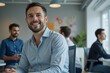 © indofootage - Portrait of a business man sitting in an office with his colleagues in the background. Happy business man working in a co-working office