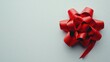 © Thirawat - A bright red gift bow with a glossy finish and textured ribbon loop rests against a smooth white background.