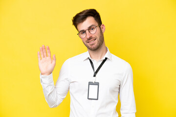 Poster - Young caucasian with ID card isolated on yellow background saluting with hand with happy expression