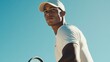 © Adi - Tennis player preparing to hit a shot, dressed in white shirt and cap under clear sky. Focused expression and athletic build emphasize concentration and physical fitness