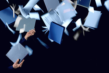 Office routine stress, hands holding two ring binders, other blue and gray folders and documents flying around, concept for management, organization and work overload, black background, copy space