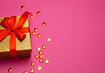 Wall Mural - golden gift box with red ribbon and heart shaped confetti creating a romantic atmosphere for valenti