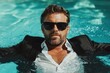 © Lens Legacy - A man comfortably reclines in a bright blue swimming pool, fully dressed in a stylish black suit and wearing dark sunglasses, conveying a sense of leisure and elegance.