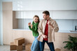 © DimaBerlin - Loving family couple have fun on moving day. Happy, overjoyed man and woman smiling dancing in empty kitchen with cardboard boxes in new purchased apartment. Pleasure of fulfilling dream goal together