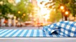 © nuiiko - Table top gingham concept. A checkered picnic blanket is laid out in a vibrant city setting, illuminated by warm sunset light and surrounded by greenery.