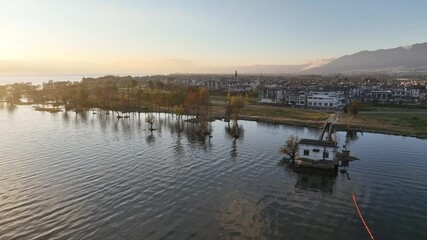 Poster - 4K aerial view of Erhai Lake in Dali, Yunnan, China at sunset.  Buildings line the shore, trees reflected in calm water.