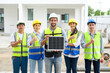 © bigy9950 - electrician man in safety vest with helmet showing solar cell panel with the team in background, standing in the under-construction building. Green energy electricity concept.