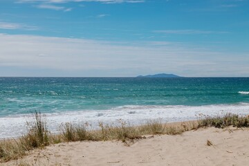 Wall Mural - Coastal beach scene with waves crashing on shore. Tranquil ocean view with distant island. Perfect for relaxation. OPOUTERE, COROMANDEL PENINSULA, NEW ZEALAND