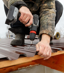 Wall Mural - A man is using a power drill to install shingles on a roof