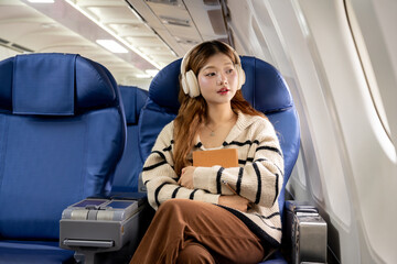 Fototapete - Asian woman sitting on airplane listening to music and writing diary while traveling somewhere during vacation.