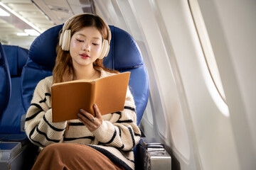 Fototapete - Asian woman sitting on airplane listening to music and writing diary while traveling somewhere during vacation.