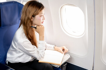 Fototapete - Asian businesswoman working during flight, taking notes in book