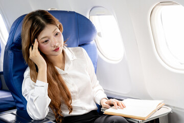 Fototapete - Asian businesswoman working during flight, taking notes in book