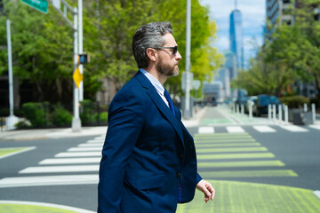 Wall Mural - Photo of business man in suits walking outdoor through city street in NY. Businessman walking and in the city. Businessman walk on the city road. Confident business man go to the new goals.