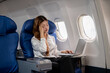 © bongkarn - Tired, overworked Asian businesswoman feels a headache while working on her laptop during the flight