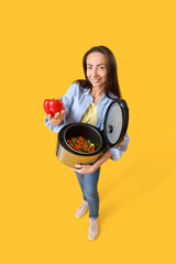 Beautiful woman with multi cooker and bell pepper on yellow background