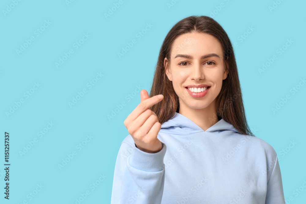 Beautiful young woman making heart gesture on blue background