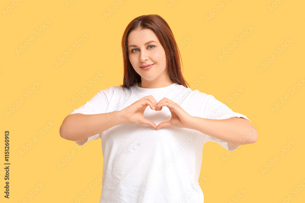 Beautiful young woman making heart gesture on yellow background