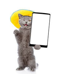 Aufkleber - Winking cat wearing summer hat standing on hind legs and showing big smartphone with white blank screen. Empty space for text. isolated on white background