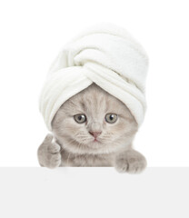 Fototapete - Cute tiny kitten with towel on it head looks above blank white banner and shows thumbs up gesture. isolated on white background